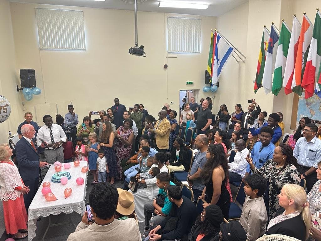 The church family gathered in the church hall, with international flags displayed on the wall
